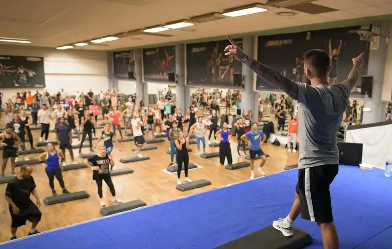 Un instructeur anime un cours collectif de step devant une salle comble